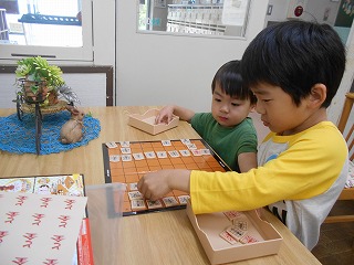 木製のテーブルで二人の男の子が横に並び、将棋の駒を真剣な表情で並べて遊ぶ様子の写真