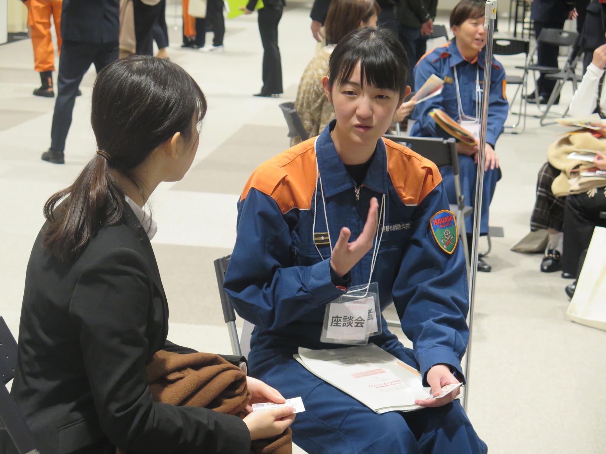 「座談会」で、消防の制服を着た女性が、対面に座った女性と身振り手振りを交えながら話している様子の写真