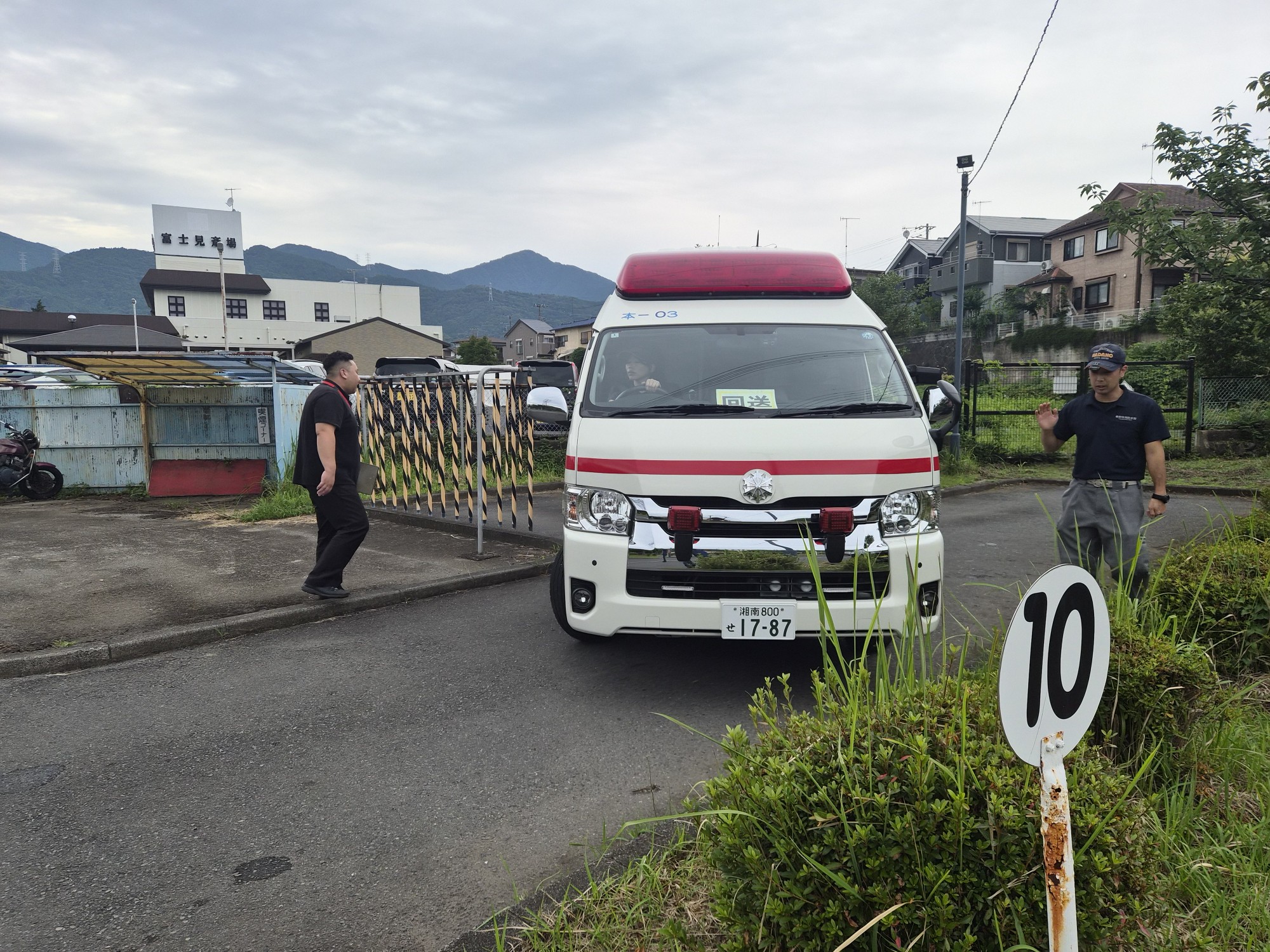 草が生い茂る空き地に停車した秦野市の救急車の後ろに、制服を着た隊員一人が立っている写真