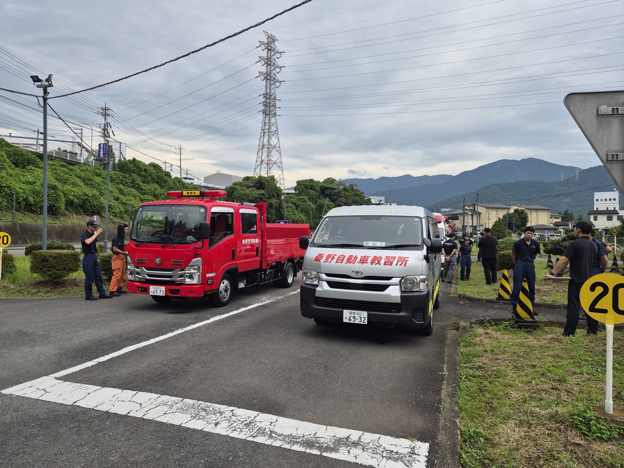 自動車教習所のようなコースで、秦野市消防本部の赤いトラックを、旗を持った隊員が後方に下がるよう誘導している訓練風景の写真
