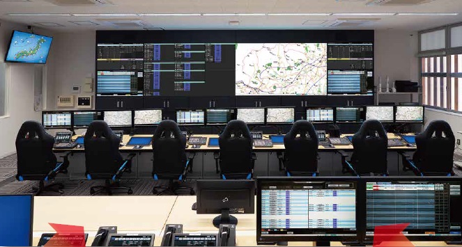 大規模な映像モニターが壁一面に並び、手前に複数のオペレーター席が配置し、近代的な管制室または指令センターの写真