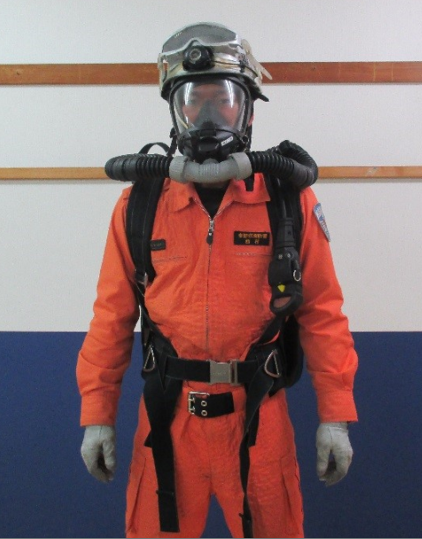 オレンジ色の救助活動服とヘルメットを着用し、フルフェイスマスクの空気呼吸器を装着した男性隊員が正面を向いて立っている全身写真