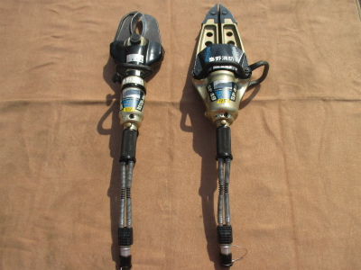 茶色の布地の上に置かれた、自動車事故などの救助活動に使用される油圧式の救助用資機材で、左側が切断用のカッターで、右側がこじ開け用のスプレッダーの2種類を並べた写真