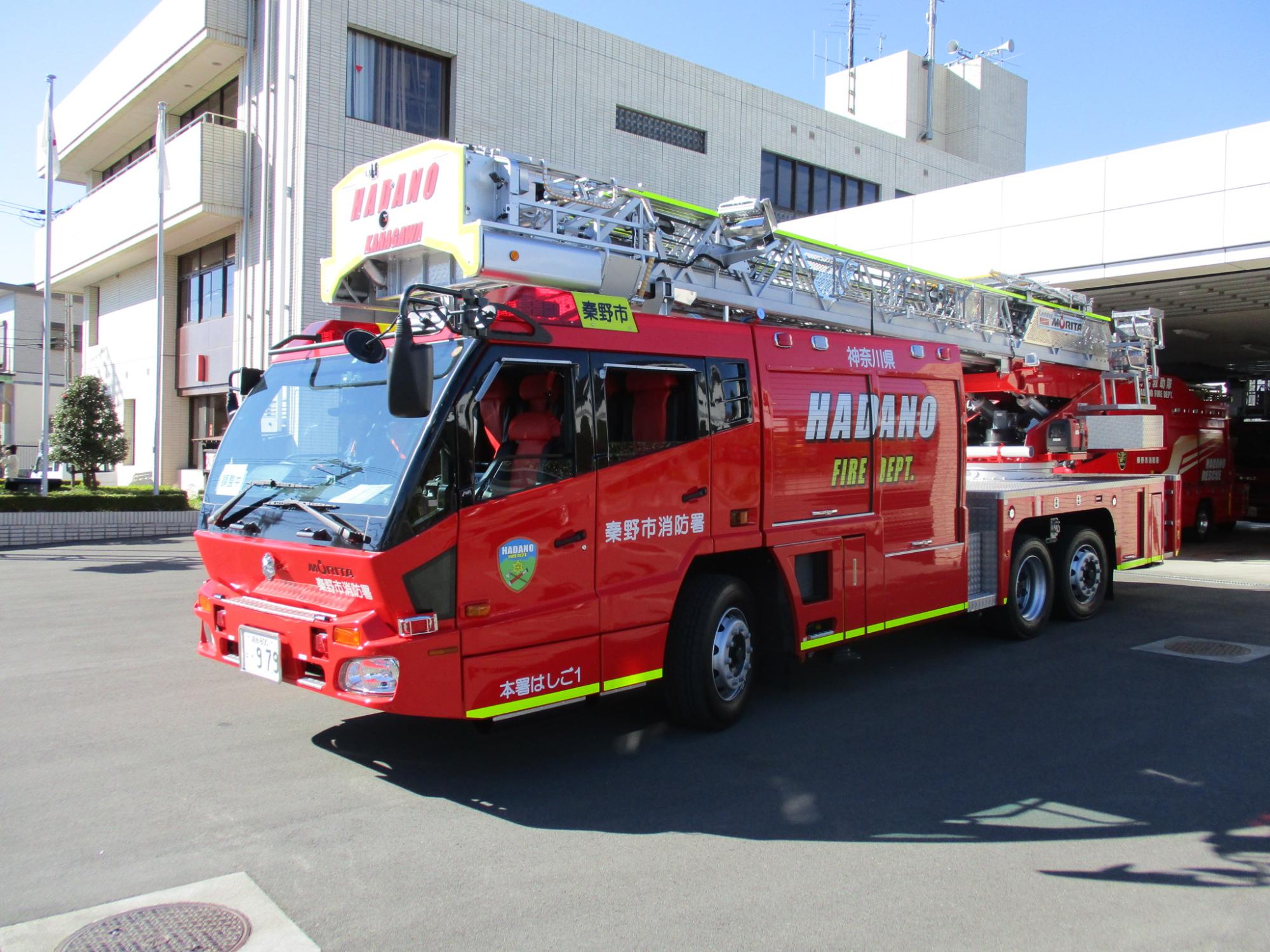 銀色の梯子を上部に搭載しており、赤い車体の下部に黄色の線が入っている消防自動車を前方斜め前から撮影した写真