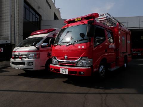 消防署の建物の前で、手前に赤い消防車、その隣に白い救急車が並んで停車している写真