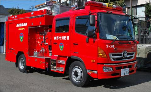 赤い車体に白文字で秦野市消防署と書かれたシャッター式の資機材収納庫と屋根の赤色灯が特徴的な水槽付消防ポンプ自動車を斜め正面より撮影した写真