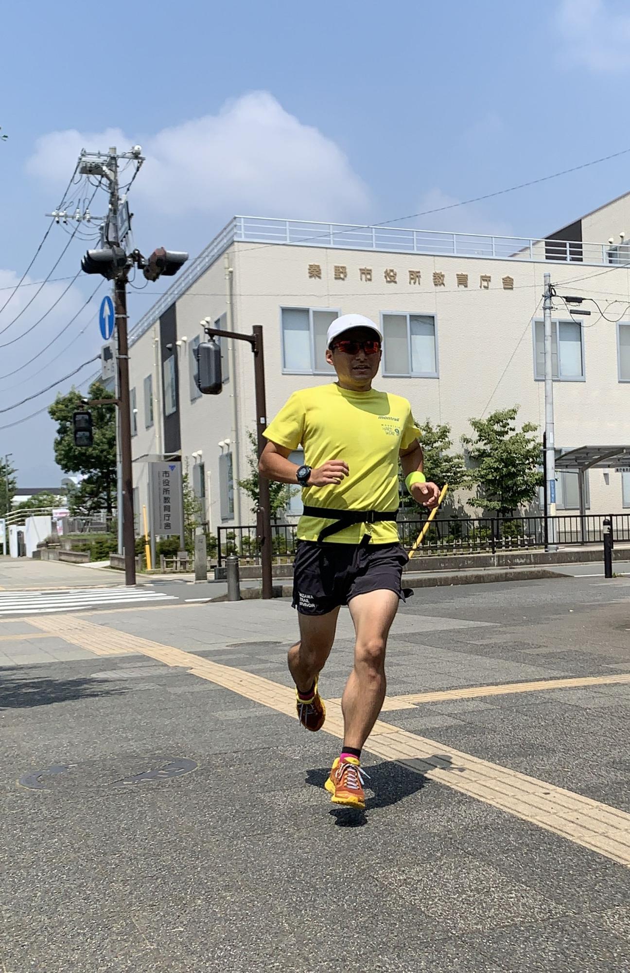 隊員グッズを着用した男性が、舗装された歩道を走っている様子を正面から捉えた写真