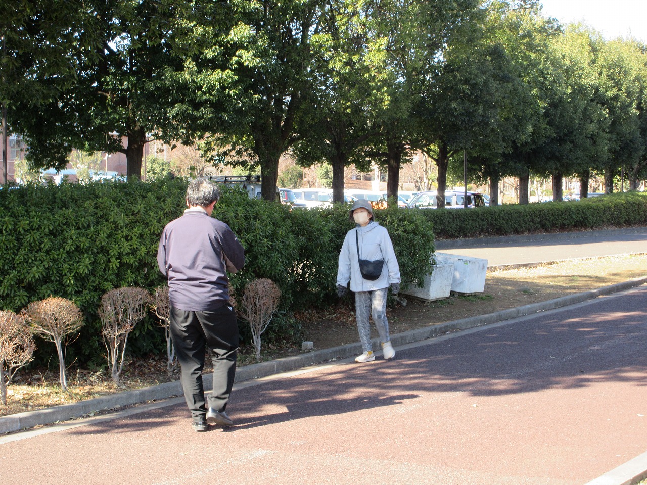 後姿の黒い服装の男性が薄い色のパーカーと帽子、マスクを着用した女性に声をかける様子の写真