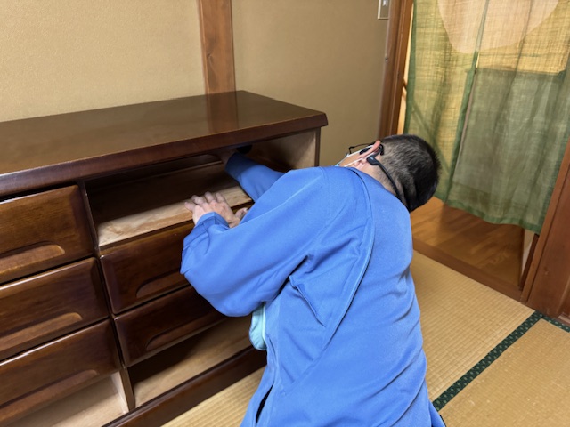 和室で青い作業服を着た人物が木製の引き出しを開けて震災時の家具転倒防止装置を設置している様子の写真
