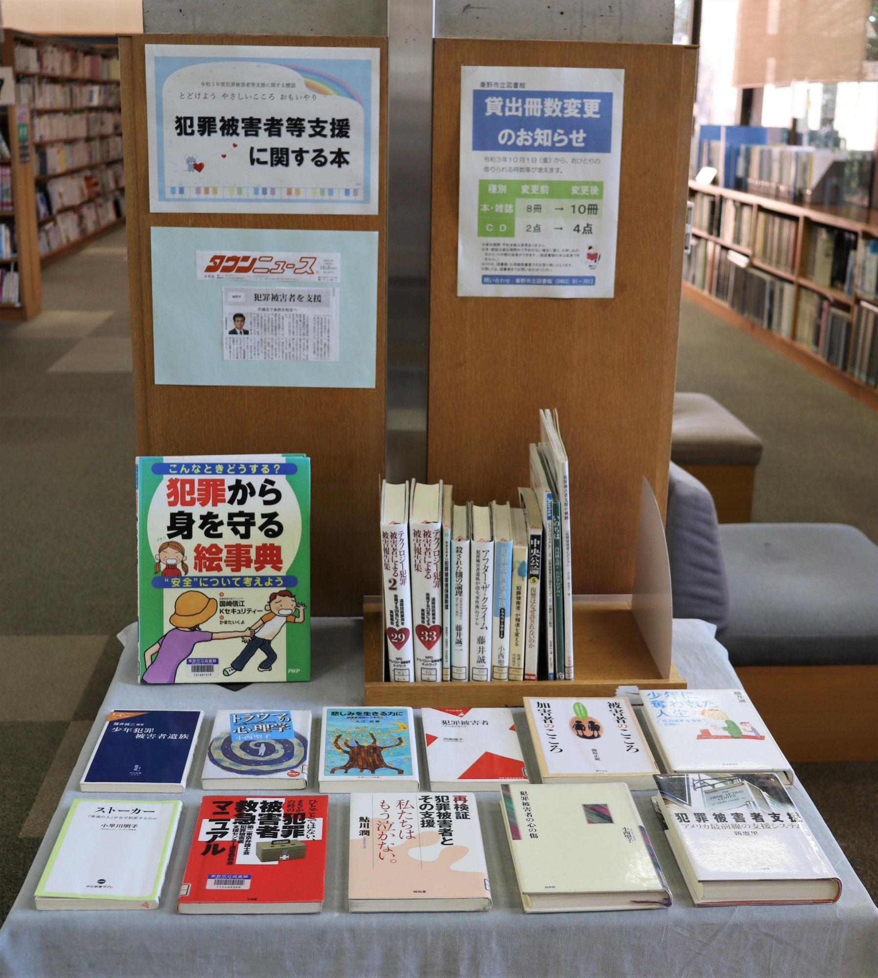 図書館内に設置された犯罪被害者等支援に関する本の特設コーナーで、木製の展示台に「犯罪から身を守る絵事典」や関連書籍が並び、背後の掲示板には貸出冊数変更のお知らせが掲示されている写真