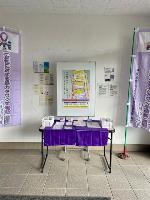 白い壁に女性支援・DV防止啓発ポスターが掲示され、紫色の布で覆われたテーブルに相談窓口案内パンフレットが配架された公共施設の女性相談窓口啓発コーナーの写
