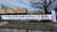 木造公共施設の外壁フェンスに「女性に対する暴力をなくす運動11月12日~11月25日」と紫リボンマークを配した白地の長尺横断幕が掲示された女性支援啓発キャンペーンの写真