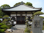 右側に大きな石碑があり、その先の手入れがされた境内の奥に、特徴的な屋根を持つ木造の極楽寺が立っている写真