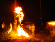 暗闇の中、オレンジ色の炎を上げて燃えるやらの山の周りに人々が集まっている、下大槻百八松明の一幕の写真