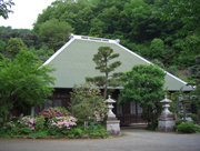手入れされた植栽と一対の石灯籠の奥に、緑の木々に囲まれた、薄い緑色の屋根の自興院が建っている写真