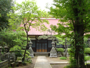 緑の木々や植栽が両脇に並んだ石畳の道の先に一対の石灯籠が置かれ、その後ろに赤い屋根の龍法寺が建っている写真