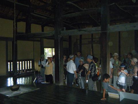 たくさんの人々が、天井が高い古い日本家屋の薄暗い室内を見学している写真