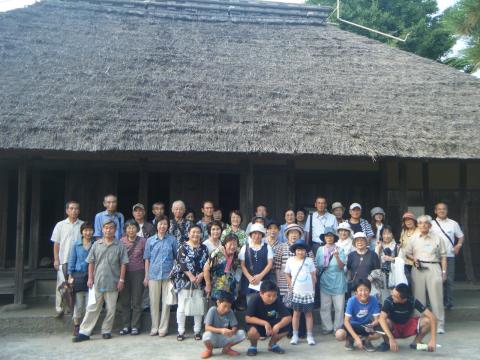 古い茅葺屋根の日本家屋の前で、たくさんの参加者たちが並んで写した集合写真