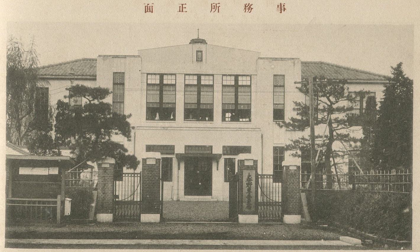 大きな建物と門が正面に写っており、門柱には看板が取り付けられている、秦野専売局のモノクロ写真