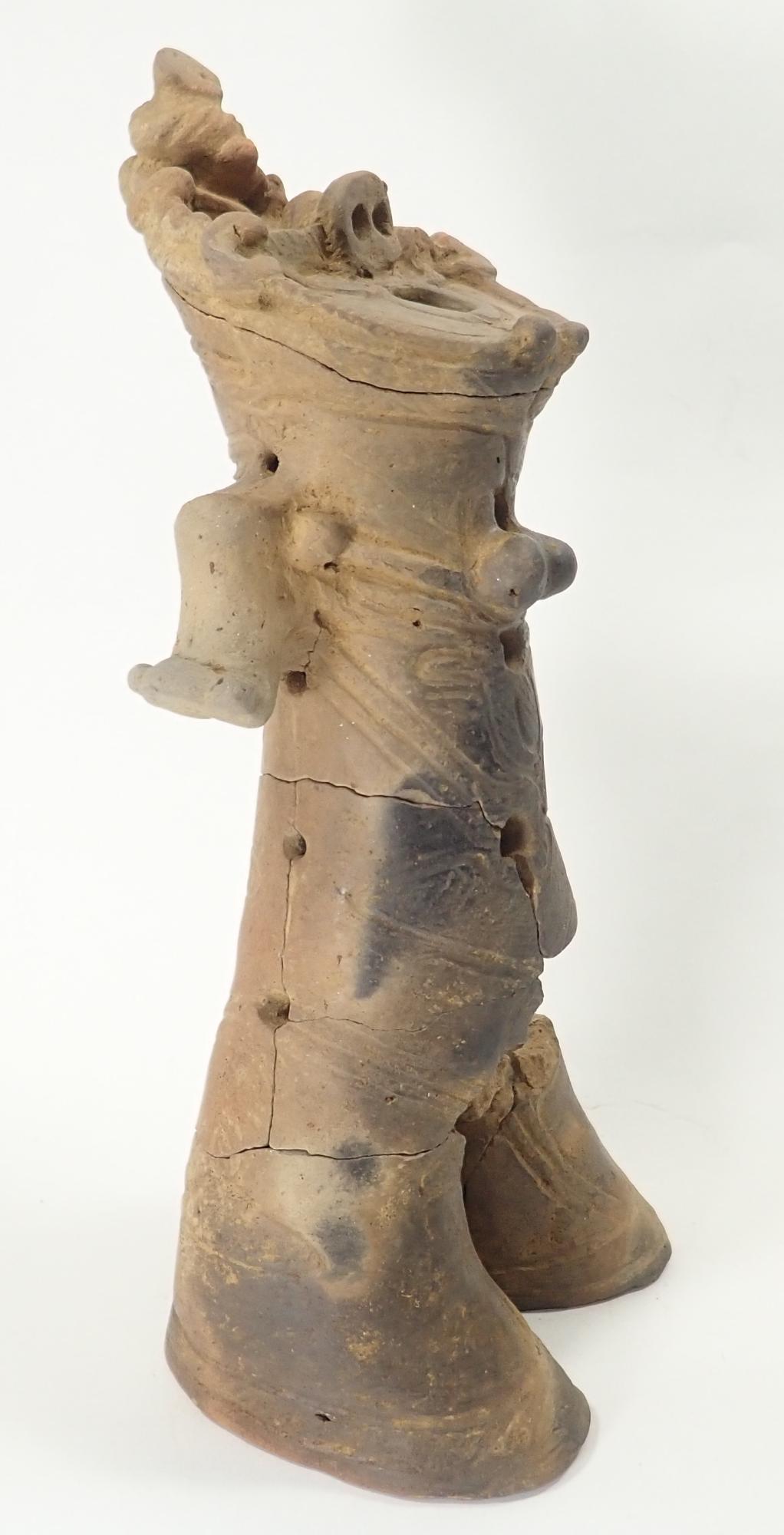 茶色の土器でできた、ひび割れや一部欠損がある土偶を横から撮影した写真