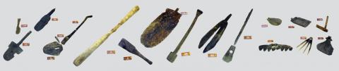 大小様々な形の農具が横一列に並んでおり、シャベルや棒状のような道具などが展示されている写真