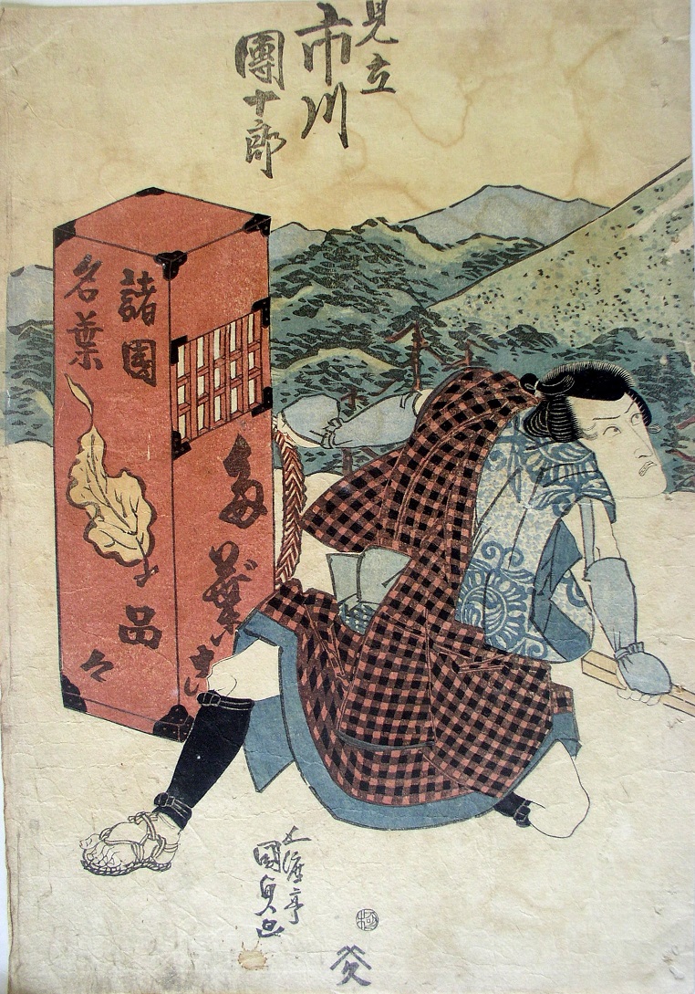 山を背景に、赤い市松模様の羽織を肩にかけた男が、地面に座り込みながら背後に名薬の文字が書かれた大きな箱を担ごうとしている浮世絵