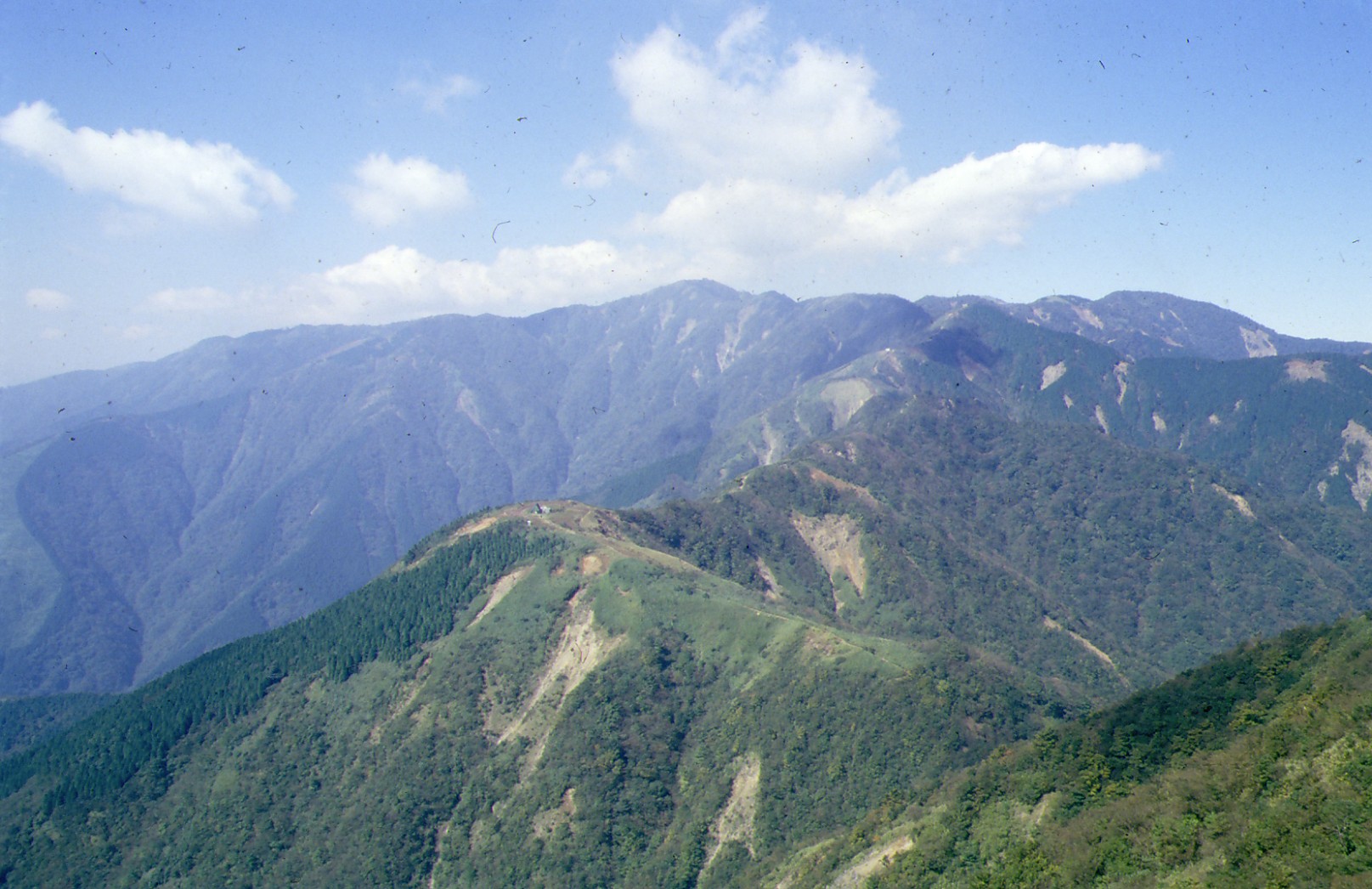 緑の木々に覆われ、ところどころ土砂がむき出しになった山々が連なっている風景の写真