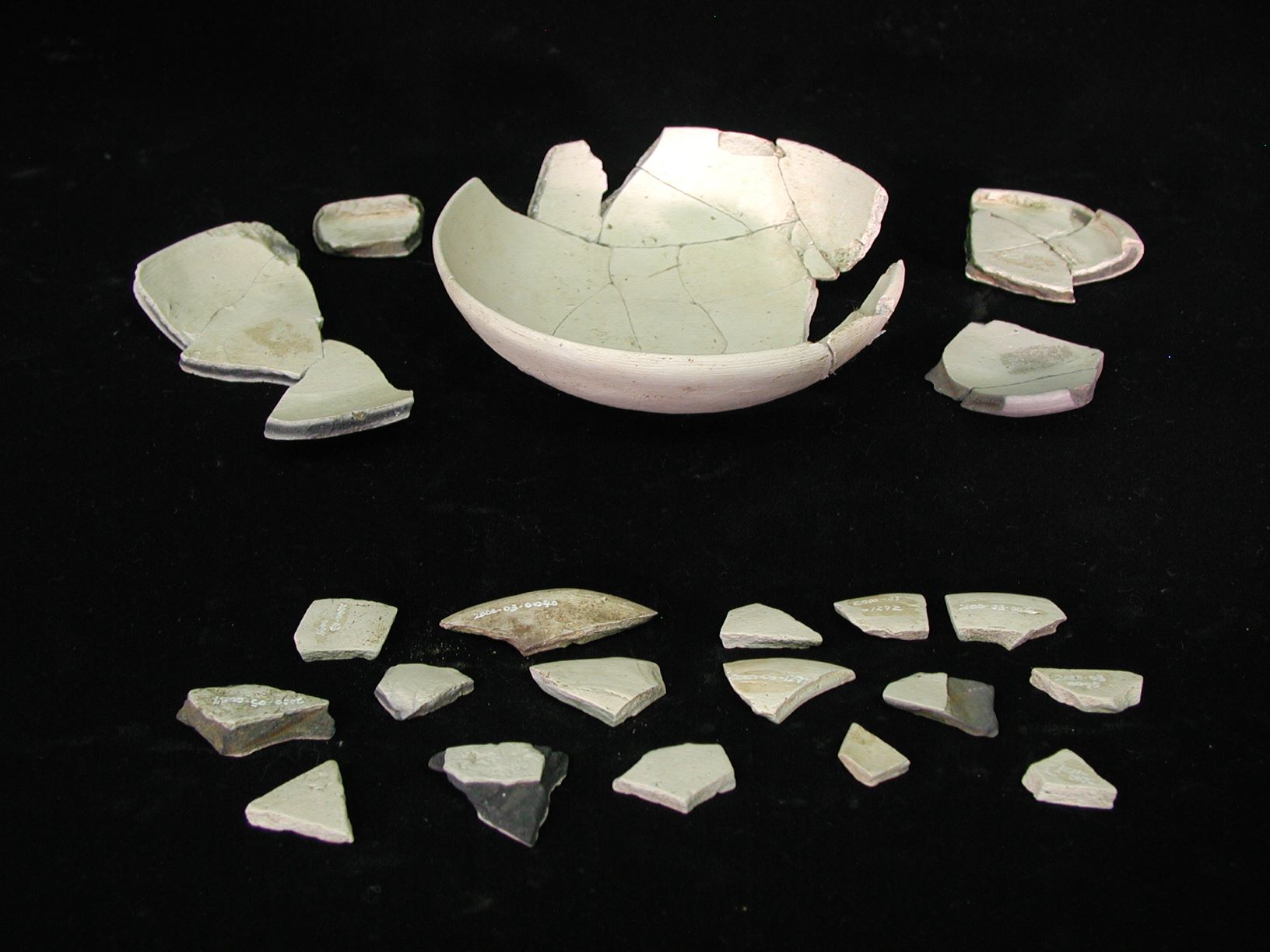 いくつかの破片に割れた白い陶器の鉢と、多数の小さな破片が並べられている写真