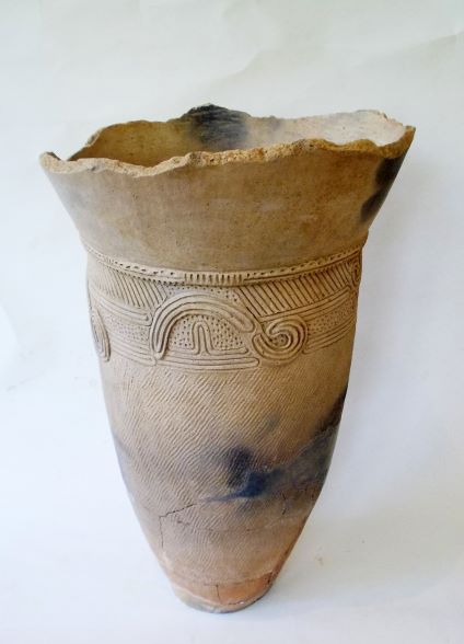 首のあたりが外側に広がり、表面に渦巻き模様や波線、細かい線が刻まれ、一部に焦げのような黒い跡がある状態の土器の写真