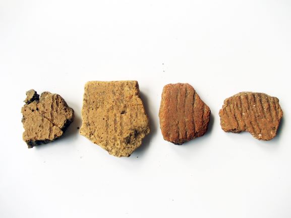 異なる土器の破片で構成され、表面に縄文時代特有の縄目模様や道具で刻まれた線模様が見られる4点の縄文土器片の写真