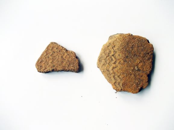 二つの破片になった薄茶色の土器が並べられており、右側の破片には波のような文様が刻まれている写真