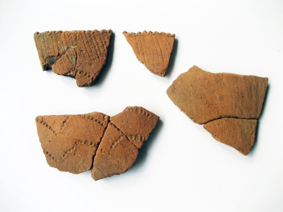 点線や縄目のような文様が刻まれた薄茶色の土器の破片が4つ置かれている様子の写真