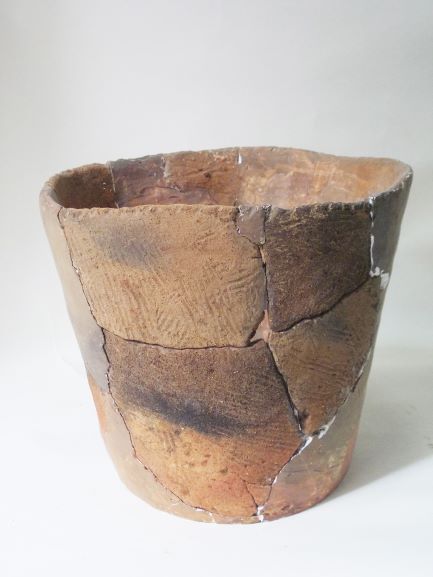 表面に斜線模様が刻まれた複数の破片をつなぎ合わせて修復された状態の深鉢形の土器の写真