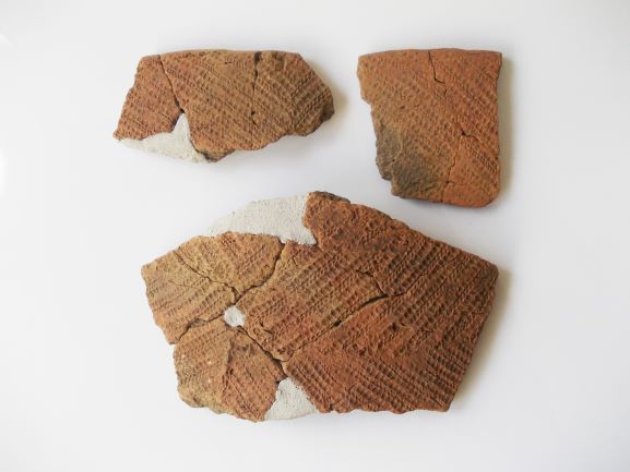 網目模様が刻まれた薄茶色の土器の破片が3つ置かれている様子の写真