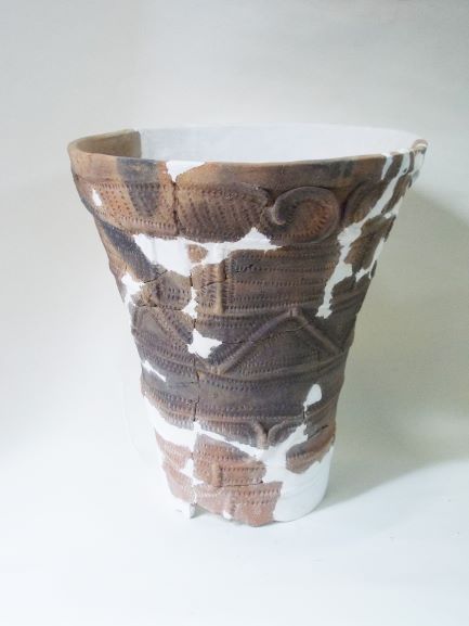 白い補修材でつなぎ合わされた、深鉢形で、表面には四角や三角の模様が複雑に施されている土器の写真