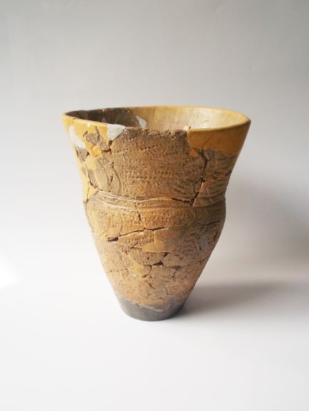 複数の破片をつなぎ合わせて修復された、深鉢で、表面には網目や波のような文様が複雑に施されている黄土色の土器の写真