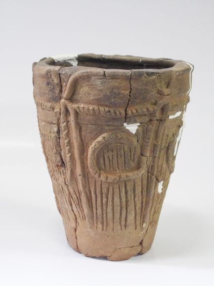 数か所を白い補修材でつなぎ合わされた、深鉢形で、表面には縄目や縦線など文様が複雑に施されている土器の写真