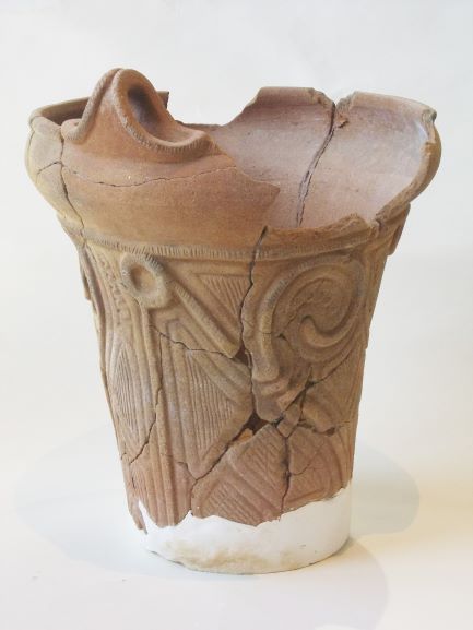 底が白い補修材でつなぎ合わされた、深鉢形で、表面には渦巻きや直線の模様が複雑に施されている土器の写真