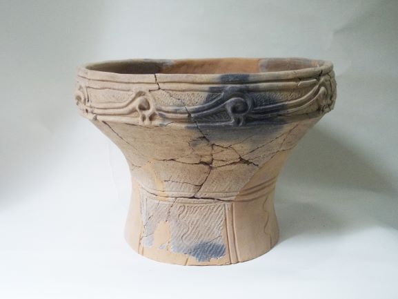 複数の破片を組み合わせて修復された深鉢形で、表面に直線や波のような文様が複雑に施されている土器の写真