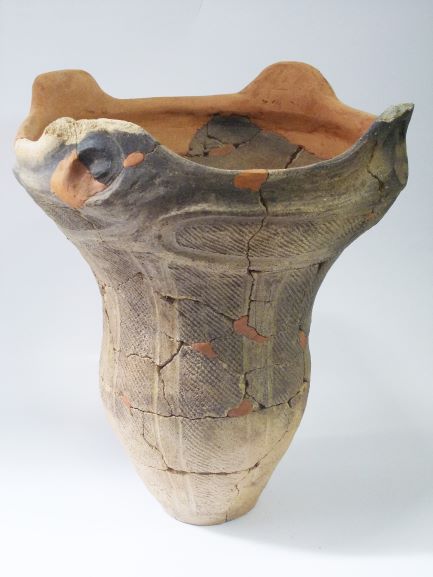 複数の破片を組み合わせて修復された、深鉢形で、口部分が4つの突起がある波形をしている土器の写真