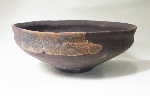 深茶色の鉢型で、欠損が補修された土器の写真