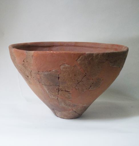修復された、赤茶色で、上部が大きく開いた碗状の形をした土器の写真