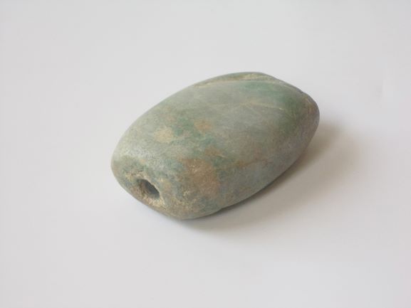 薄い緑色で、表面が滑らかに磨かれた、端に小さな穴が開けられている楕円形の石の写真