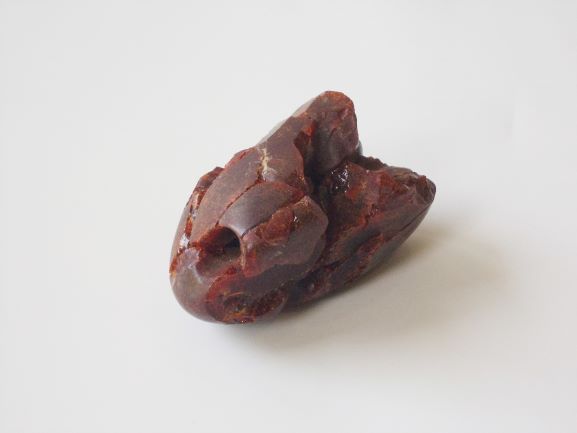 ヒビや欠損がみられる、赤茶色で端に小さな穴があけられている石の写真