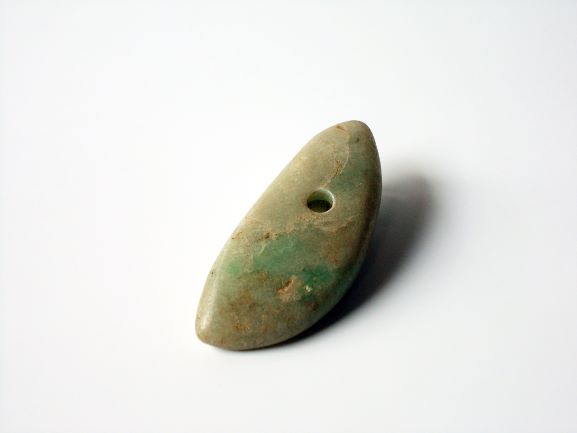 薄い茶色と緑色が混ざり合った色で、中央付近に小さな丸い穴が開けられている両端が先細りになった楕円形の石の写真