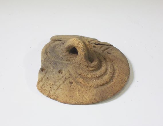 円型で、丸や波線が彫り込まれ、中央に突き出した突起に小さな穴が開いている土器の蓋の写真