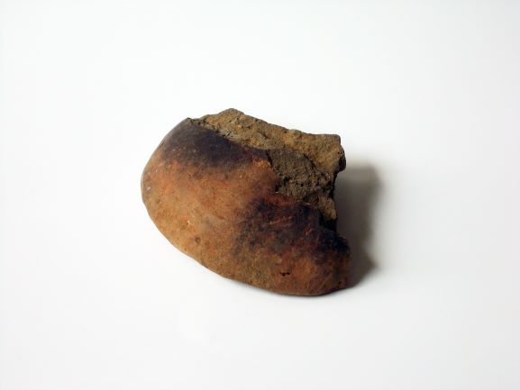 表面が一部黒く焦げたように変色し、全体的に丸みを帯びた形状をしている土器の蓋の破片の写真