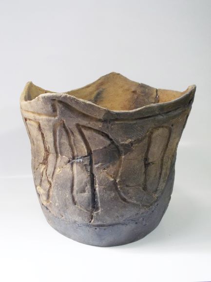 複数の破片を組み合わせて修復された深鉢形で、上部が波打ったような形をしており、複数の文様が施されている土器の写真