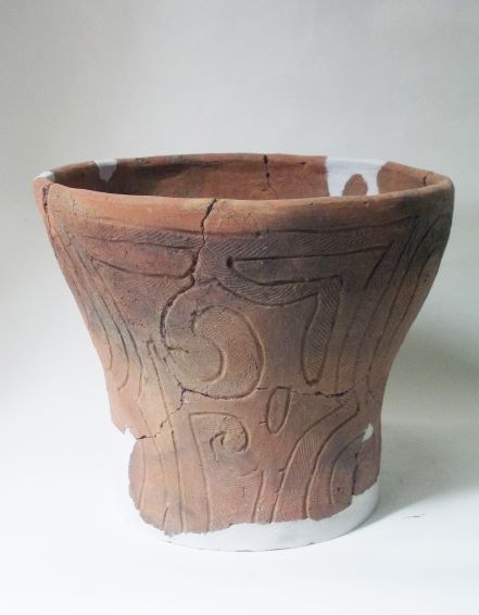 白い補修材でつなぎ合わされた、深鉢形で、表面には線で模様が施されている土器の写真