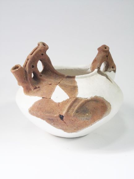 ほとんどが白い修復跡で覆われた、口縁部に2本の持ち手のような突起があり注ぎ口がある注口土器の写真